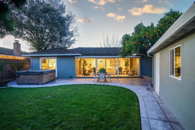 back house at dusk featuring a yard, a hot tub, and a patio area