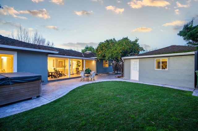 back house at dusk featuring a lawn, a hot tub, and a patio