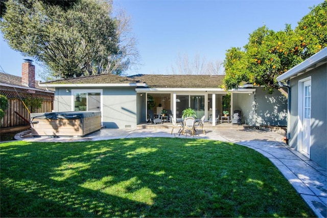 rear view of house with a hot tub, a patio area, and a lawn