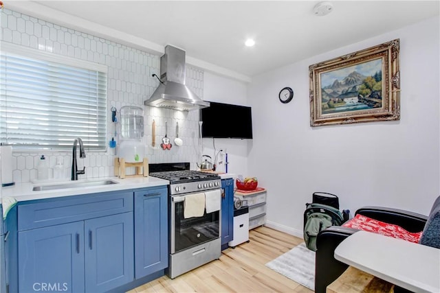 kitchen featuring sink, stainless steel gas stove, range hood, light hardwood / wood-style floors, and decorative backsplash