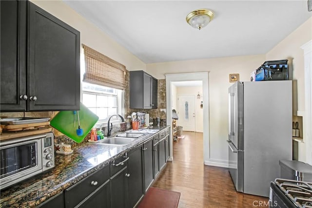 kitchen with sink, dark stone countertops, stainless steel appliances, hardwood / wood-style floors, and backsplash