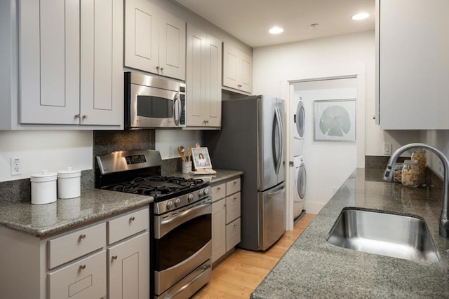 kitchen with sink, light hardwood / wood-style flooring, stainless steel appliances, stacked washer / drying machine, and white cabinets