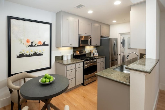 kitchen with stacked washer and dryer, sink, light hardwood / wood-style flooring, dark stone counters, and stainless steel appliances