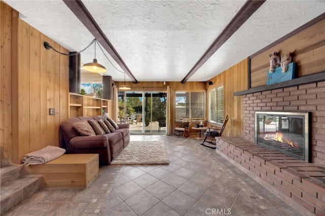 living room featuring beam ceiling, a fireplace, a textured ceiling, and wood walls