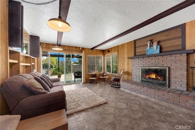 living room with a brick fireplace, a textured ceiling, beamed ceiling, and wood walls