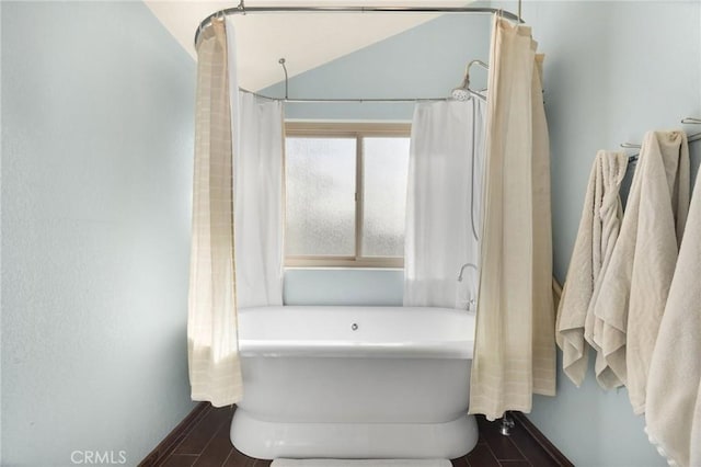 bathroom with hardwood / wood-style flooring, lofted ceiling, and a tub to relax in