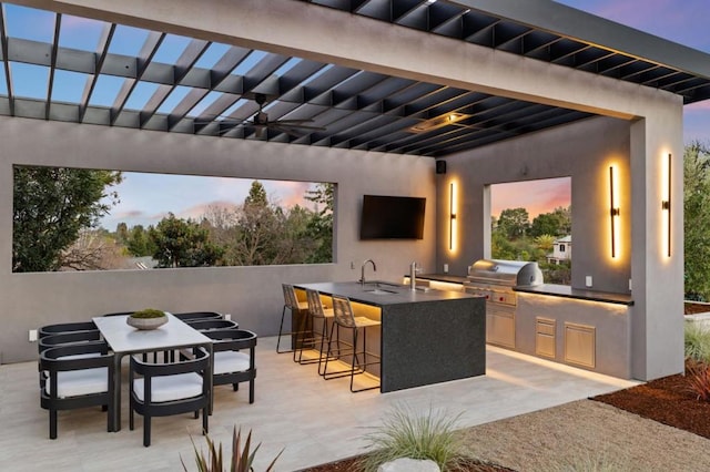 patio terrace at dusk with a grill, exterior kitchen, and a wet bar