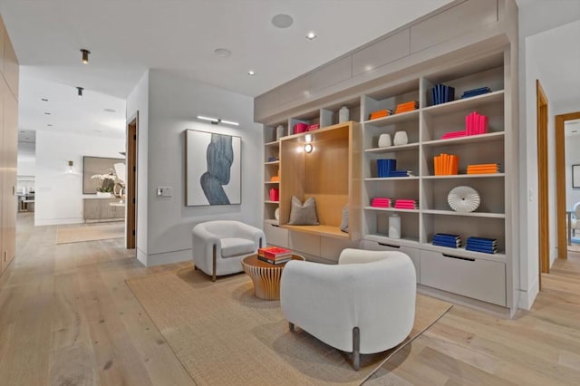 sitting room featuring built in shelves and light hardwood / wood-style flooring