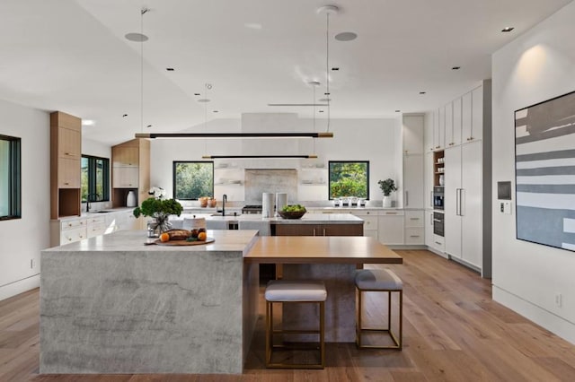 kitchen with a large island, decorative light fixtures, white cabinets, and light wood-type flooring