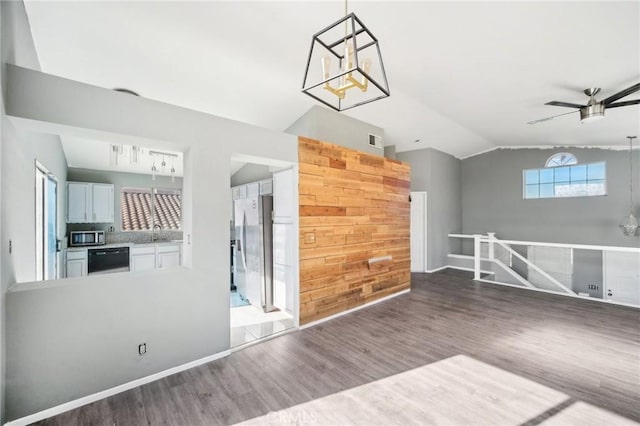 unfurnished living room with sink, hardwood / wood-style flooring, wooden walls, ceiling fan with notable chandelier, and vaulted ceiling