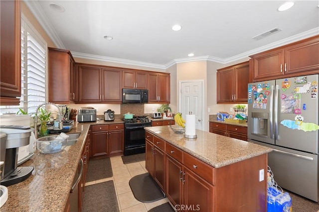 kitchen with light stone countertops, sink, black appliances, and a center island