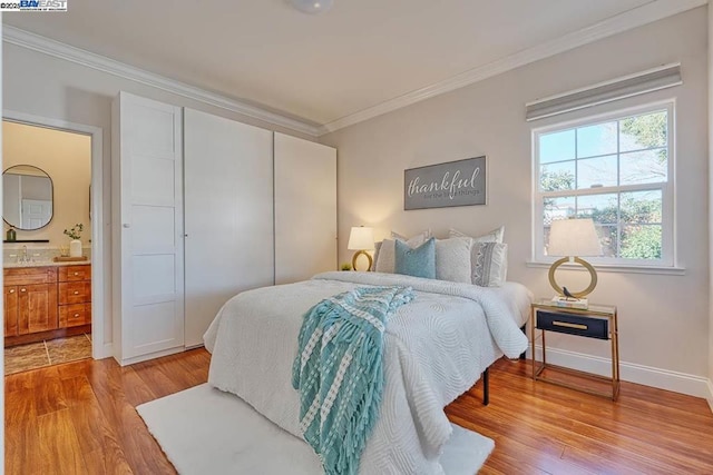 bedroom featuring ornamental molding, connected bathroom, light wood-type flooring, and a closet