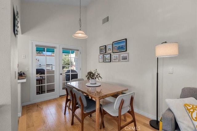 dining space with light wood finished floors, a high ceiling, visible vents, and baseboards