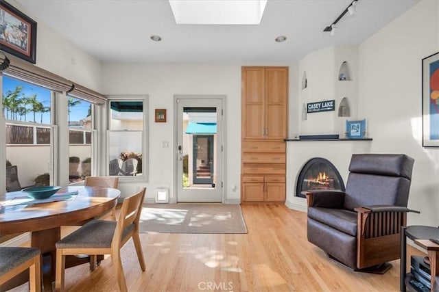 sitting room featuring a skylight, rail lighting, light wood-style floors, and a glass covered fireplace