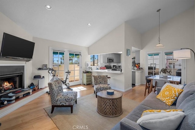 living area with light wood-style floors, recessed lighting, a warm lit fireplace, and high vaulted ceiling