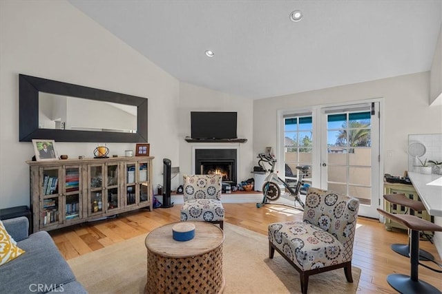 living area with lofted ceiling, a lit fireplace, recessed lighting, and light wood-style floors