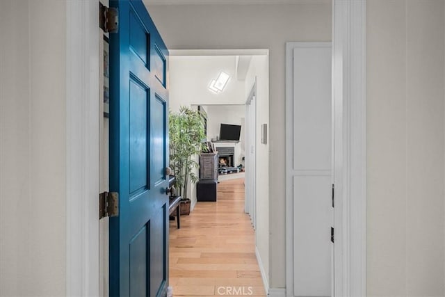 foyer entrance featuring a warm lit fireplace and light wood-style flooring