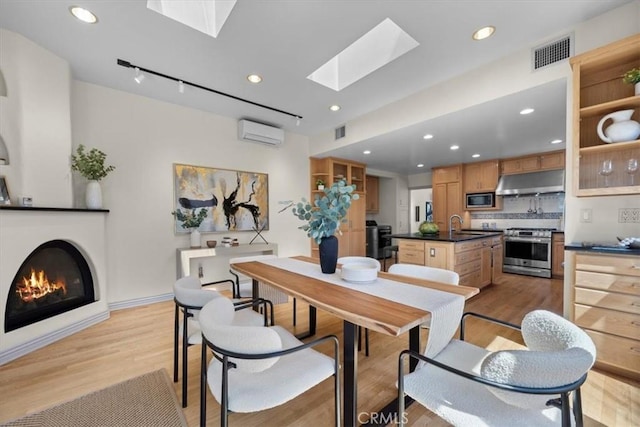 243 Park Ave, Long Beach, CA 90803 - dining space with a wall mounted air conditioner, a skylight, light wood-type flooring, a glass covered fireplace, and recessed lighting