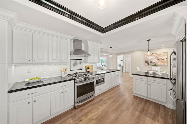 kitchen with white cabinetry, appliances with stainless steel finishes, hanging light fixtures, and wall chimney range hood