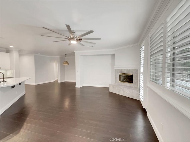 unfurnished living room featuring dark hardwood / wood-style flooring, crown molding, a tile fireplace, and ceiling fan