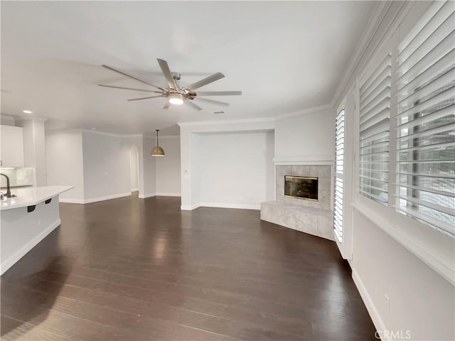 unfurnished living room featuring baseboards, a tiled fireplace, dark wood finished floors, and crown molding