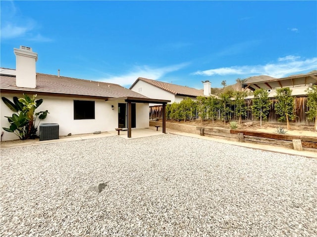 rear view of house with a patio, a chimney, fence, central AC, and stucco siding