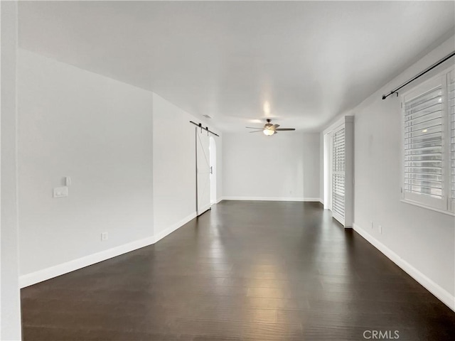 unfurnished room featuring a ceiling fan, baseboards, dark wood-style floors, and a barn door