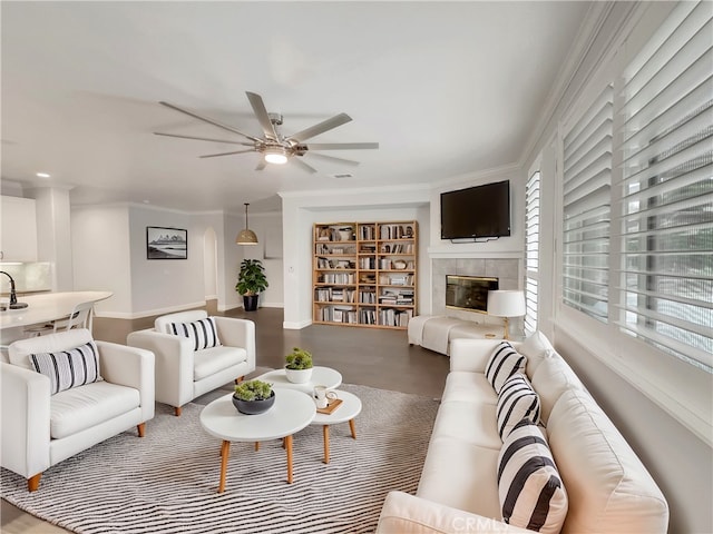 living room with sink, ceiling fan, wood-type flooring, ornamental molding, and a tiled fireplace