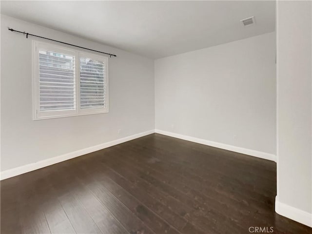 unfurnished room featuring baseboards, visible vents, and dark wood-style flooring