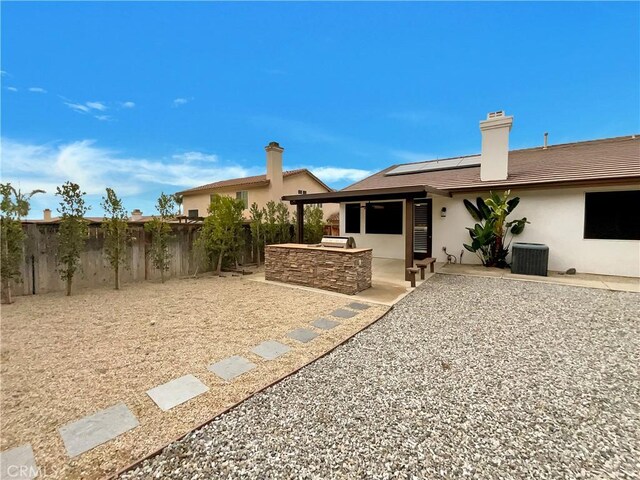 back of house featuring an outdoor kitchen, solar panels, a patio, and central air condition unit