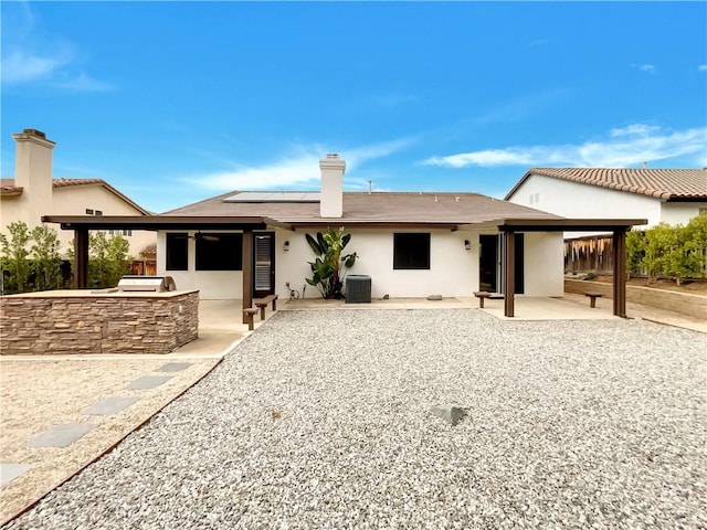 rear view of property featuring central AC unit, an outdoor kitchen, solar panels, a chimney, and a patio area