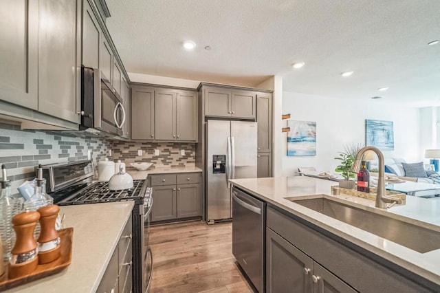 kitchen featuring tasteful backsplash, sink, gray cabinetry, stainless steel appliances, and light wood-type flooring