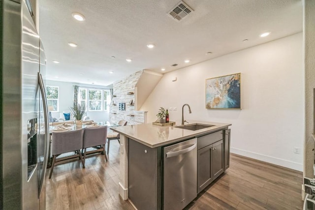 kitchen featuring dark hardwood / wood-style floors, appliances with stainless steel finishes, sink, and a kitchen island with sink