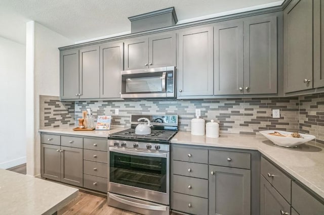 kitchen with stainless steel appliances, gray cabinets, light hardwood / wood-style floors, and backsplash