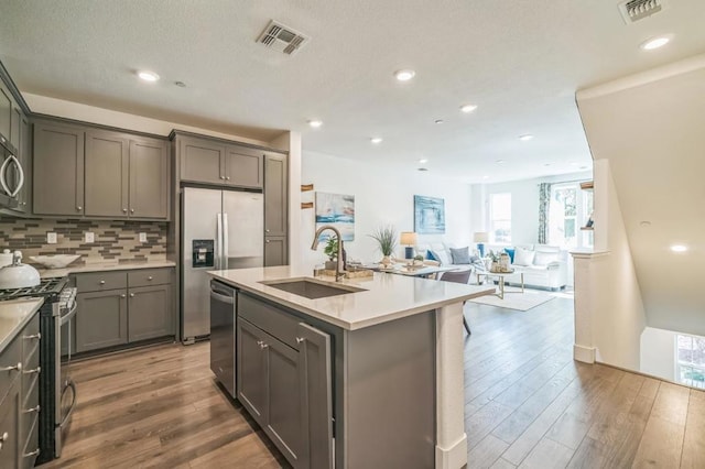 kitchen with sink, appliances with stainless steel finishes, tasteful backsplash, wood-type flooring, and an island with sink