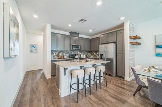 kitchen featuring appliances with stainless steel finishes, a breakfast bar, an island with sink, sink, and decorative backsplash