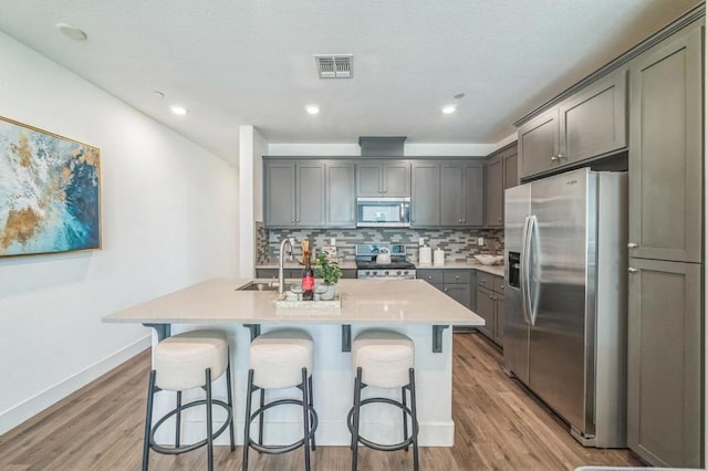 kitchen with appliances with stainless steel finishes, a kitchen island with sink, sink, and backsplash