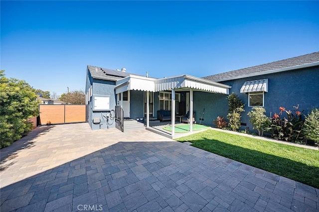 rear view of house with a patio area, a lawn, and solar panels