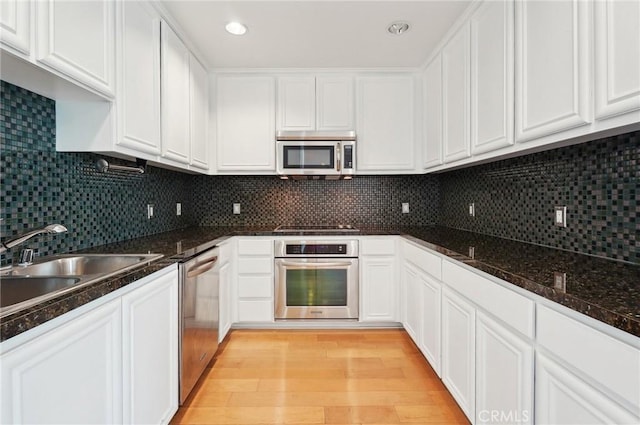 kitchen with stainless steel appliances, dark stone countertops, white cabinets, and light hardwood / wood-style floors