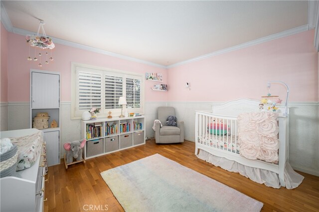 bedroom with a crib, ornamental molding, and light hardwood / wood-style floors