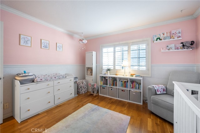 bedroom featuring ornamental molding, a wainscoted wall, and light wood finished floors