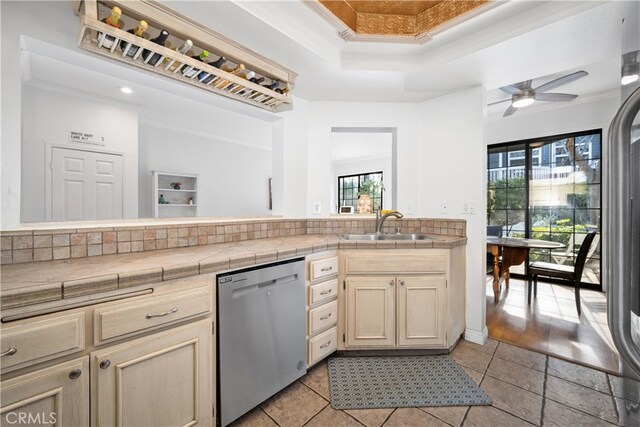 kitchen featuring tile countertops, sink, stainless steel dishwasher, and a tray ceiling