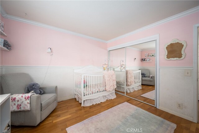 bedroom featuring hardwood / wood-style flooring, ornamental molding, a closet, and a nursery area