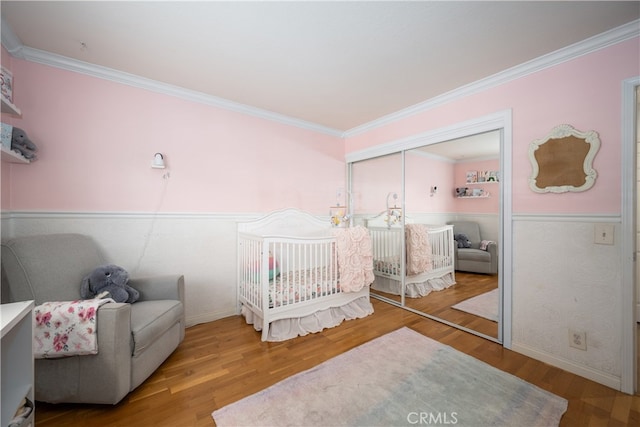 bedroom with a crib, crown molding, a closet, and wood finished floors