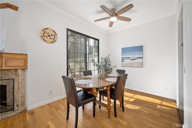 dining space featuring ornamental molding, a brick fireplace, ceiling fan, and light wood-type flooring