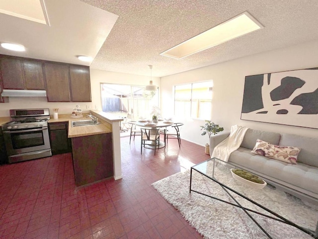 kitchen featuring sink, dark brown cabinets, stainless steel range with gas stovetop, decorative light fixtures, and kitchen peninsula