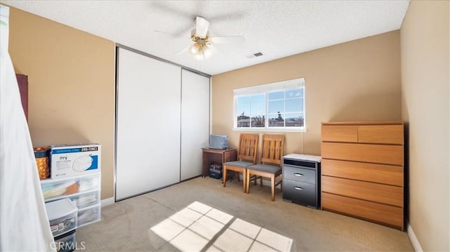 living area with ceiling fan, light carpet, and a textured ceiling