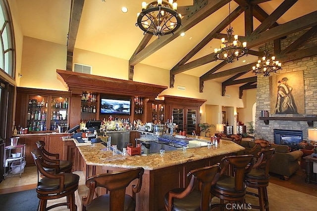 bar featuring an inviting chandelier, a stone fireplace, light stone countertops, and high vaulted ceiling