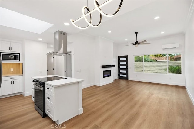 kitchen featuring black electric range oven, white cabinetry, a wall unit AC, island exhaust hood, and built in microwave