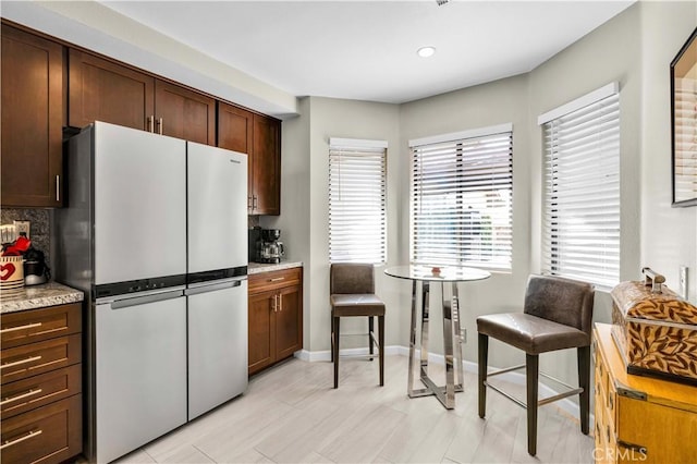 kitchen featuring tasteful backsplash, dark brown cabinets, stainless steel fridge, and light stone countertops